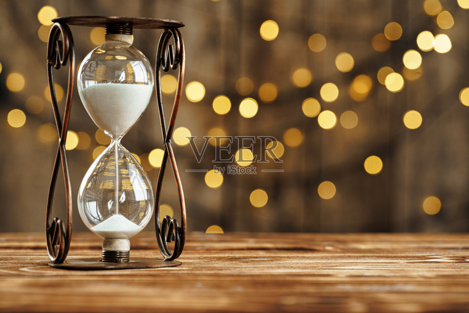 木桌上的沙漏对着模糊的灯光照片摄影图片