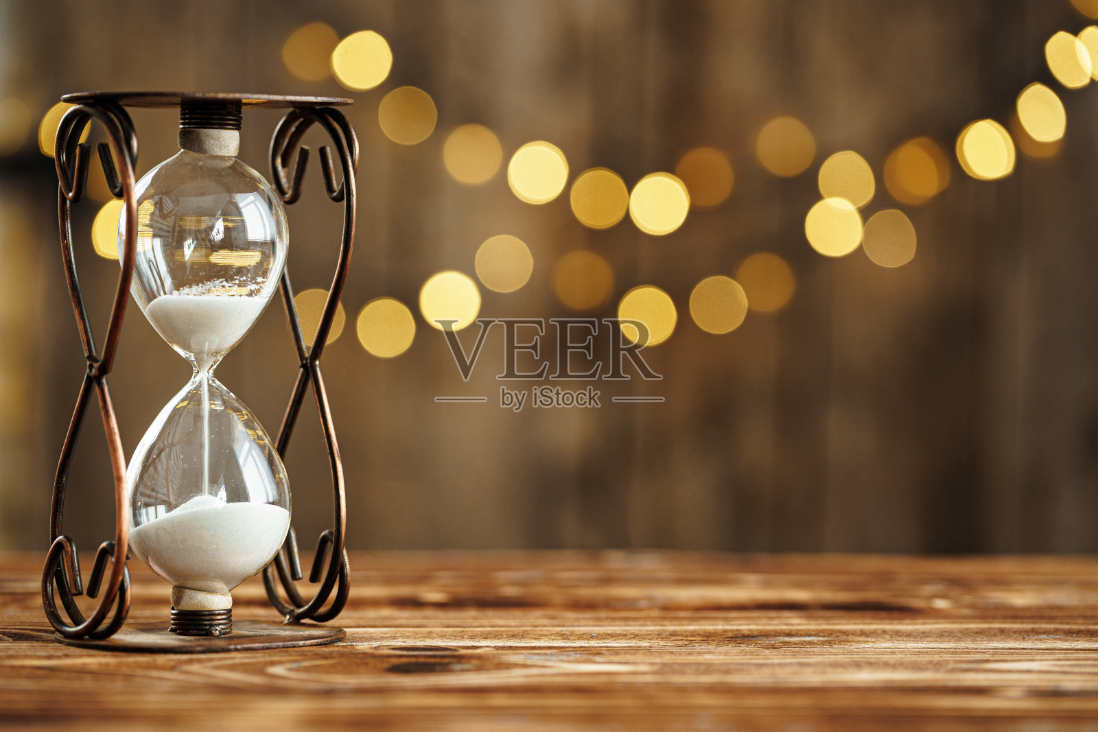 木桌上的沙漏对着模糊的灯光照片摄影图片