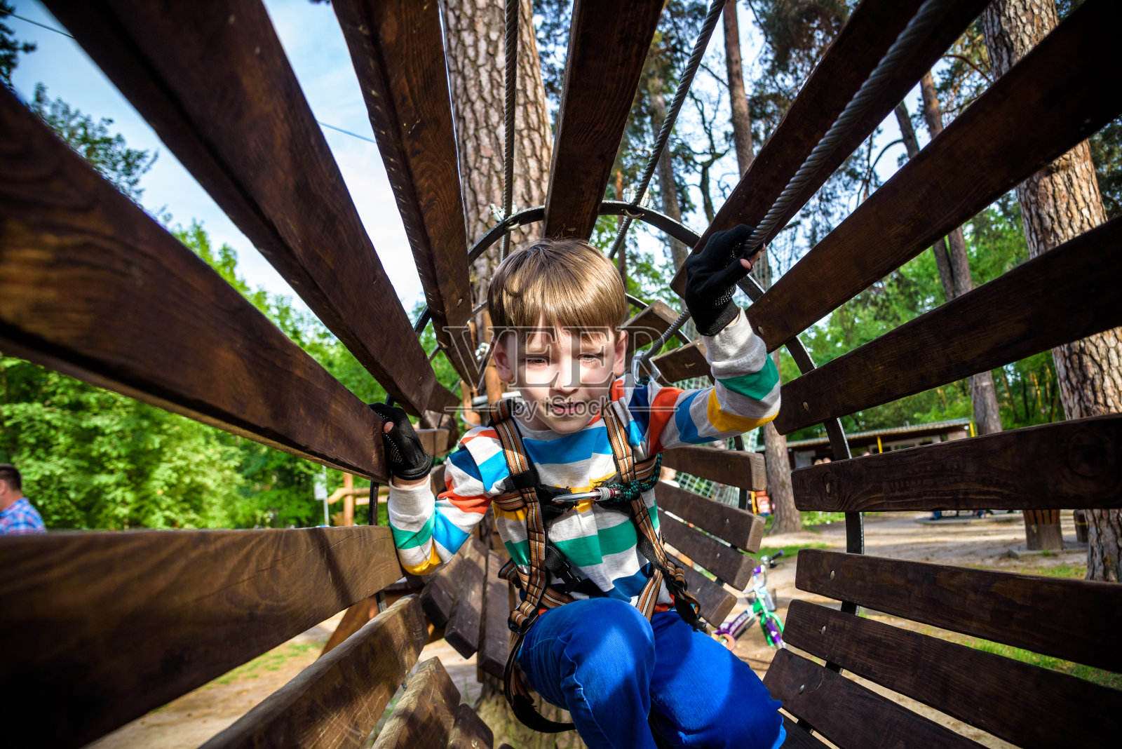 快乐的孩子克服障碍在绳索冒险公园。暑假的概念。小男孩在冒险公园玩绳子。现代儿童游乐场。户外游戏。照片摄影图片