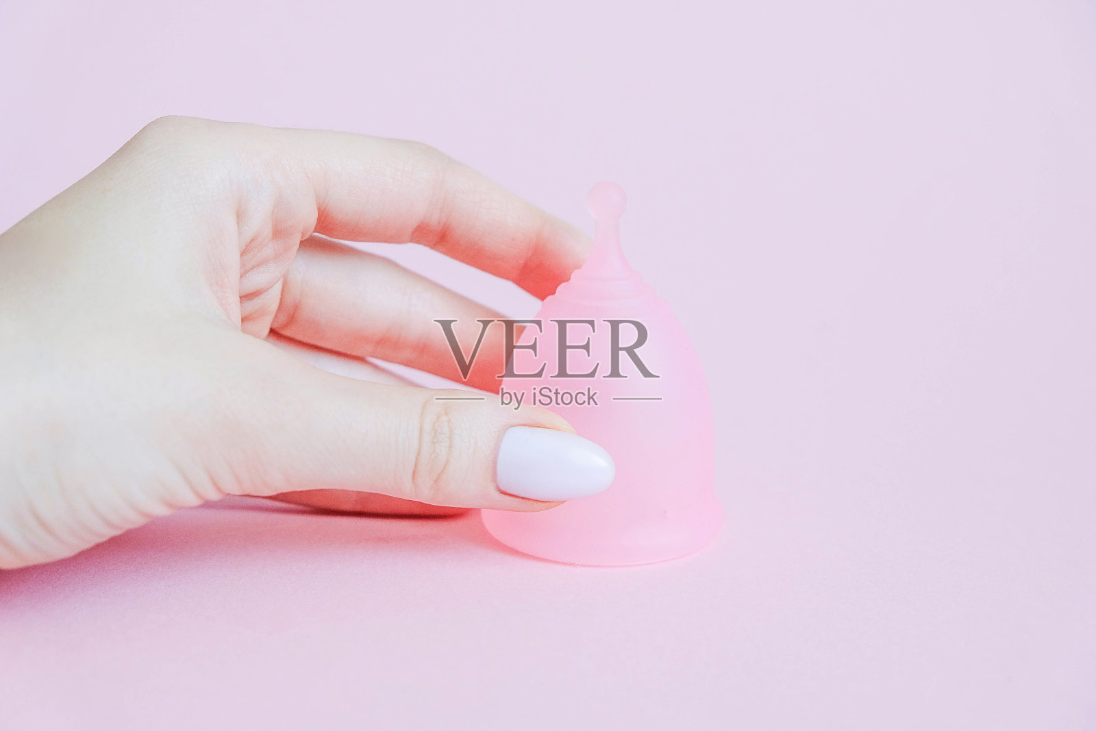 年轻女子手拿月经杯。粉红色背景的月经杯。在此期间可选择的女性卫生用品。女性健康概念照片摄影图片