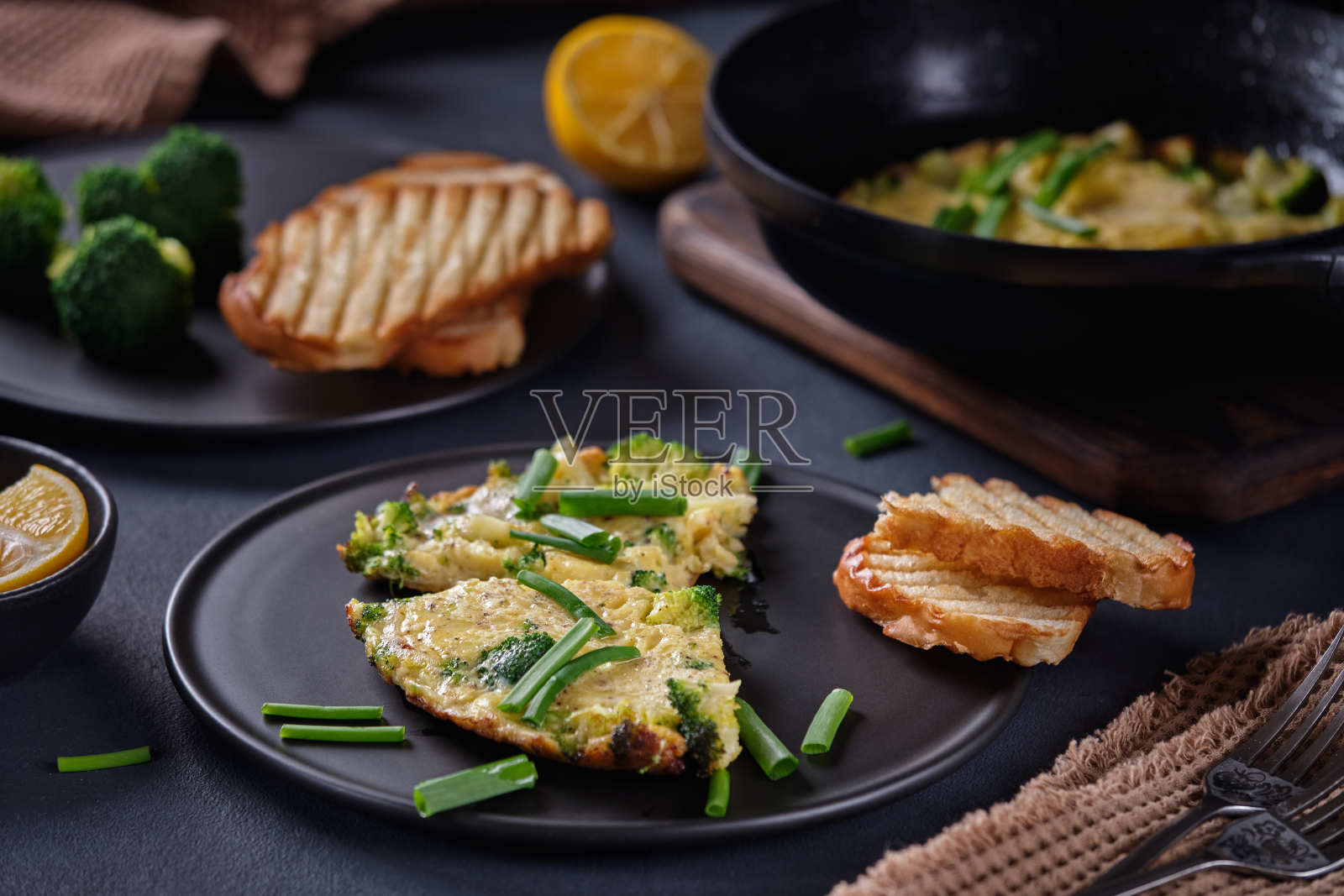 用黑色的盘子和平底锅在黑色的背景上煎，配上西兰花和葱照片摄影图片