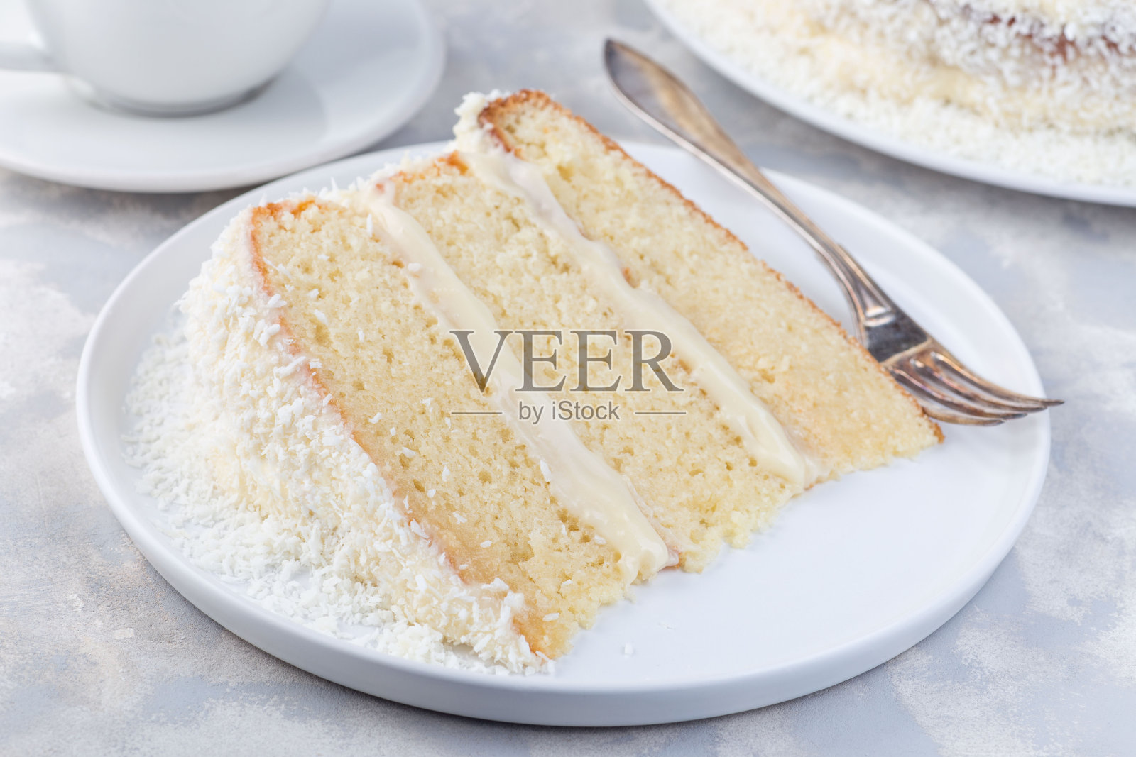 一块自制的椰子蛋糕，上面有奶油芝士糖霜和椰子片装饰，放在白色盘子上，横着照片摄影图片