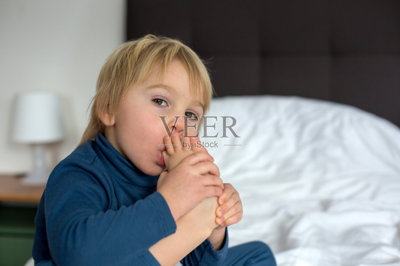 可爱的金发小孩，吮着大拇指，做着鬼脸照片摄影图片