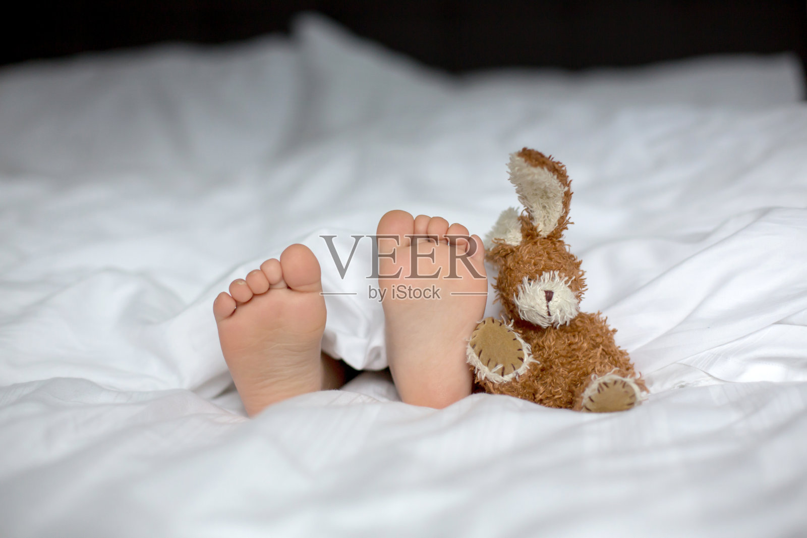 蹒跚学步的小孩的脚在前景，可爱的孩子，躺在床上，玩着小玩具照片摄影图片