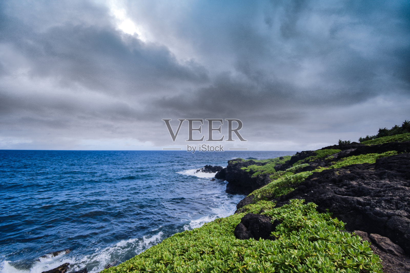 在夏威夷的太平洋海岸，杂草丛生，岩石丛生，天空阴云密布照片摄影图片