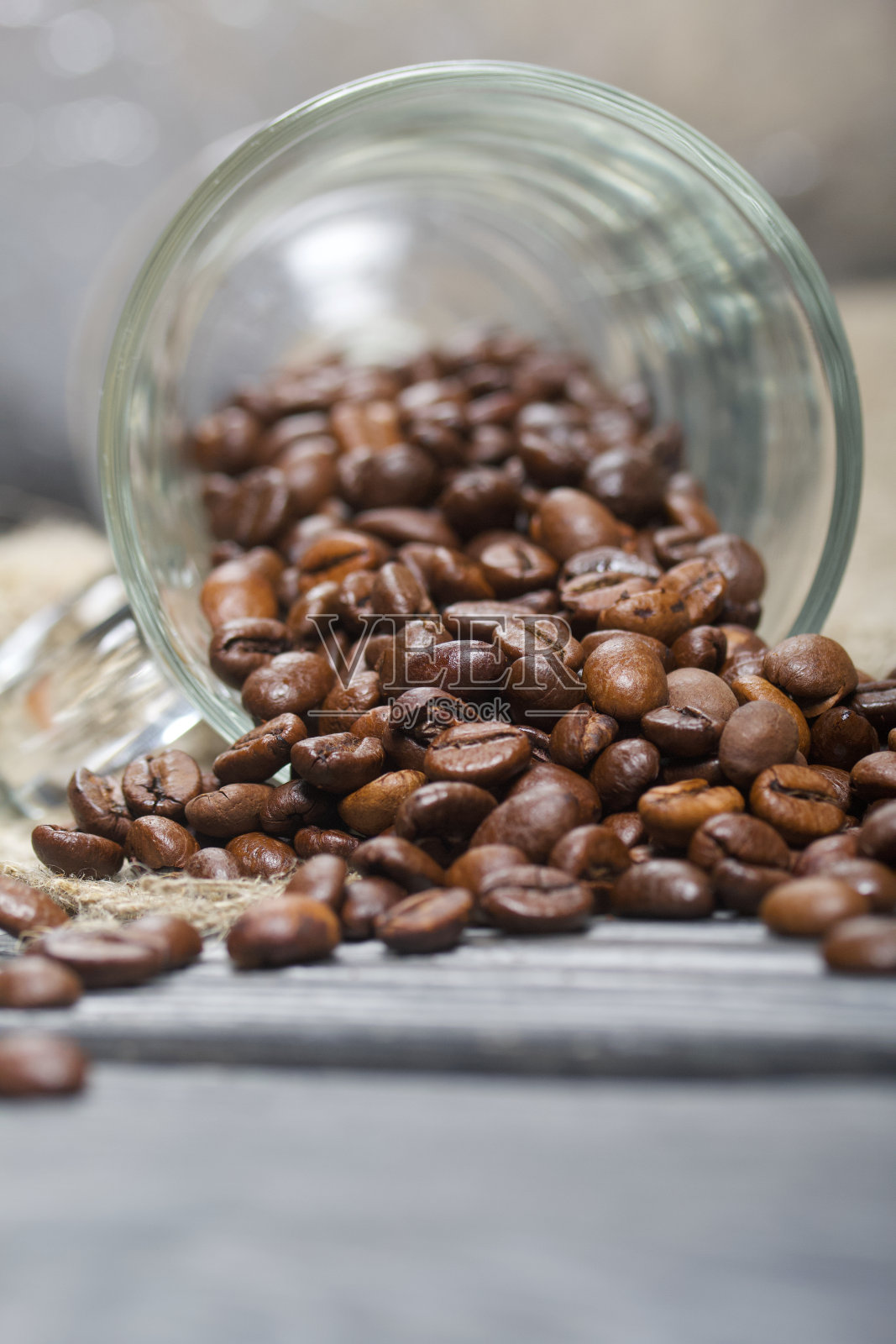 用咖啡豆打翻了玻璃杯。咖啡豆散落在亚麻布和松木板上。特写镜头。照片摄影图片