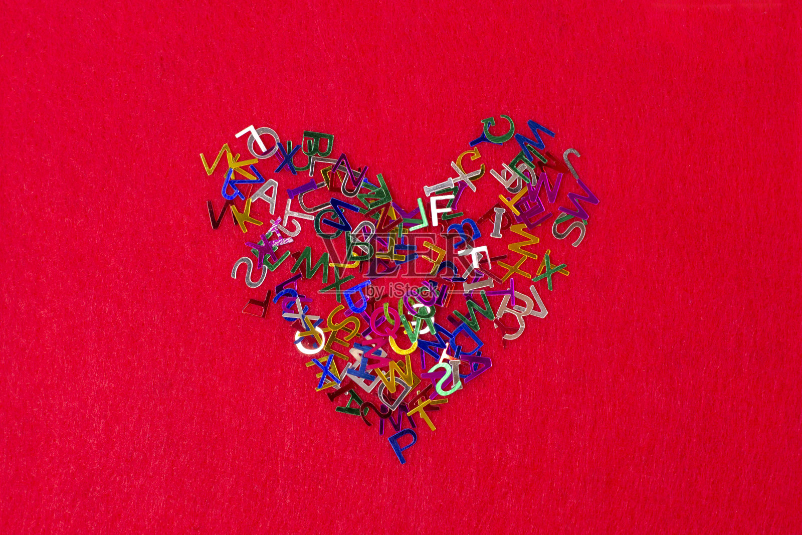 鲜艳的五颜六色的小字母散落形状的心泉在红色的背景上照片摄影图片