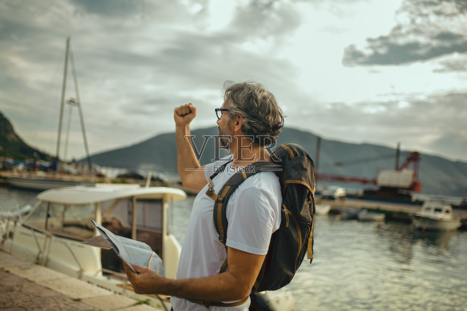 微笑的游客成熟的男子站在地图和背包靠近海边。照片摄影图片