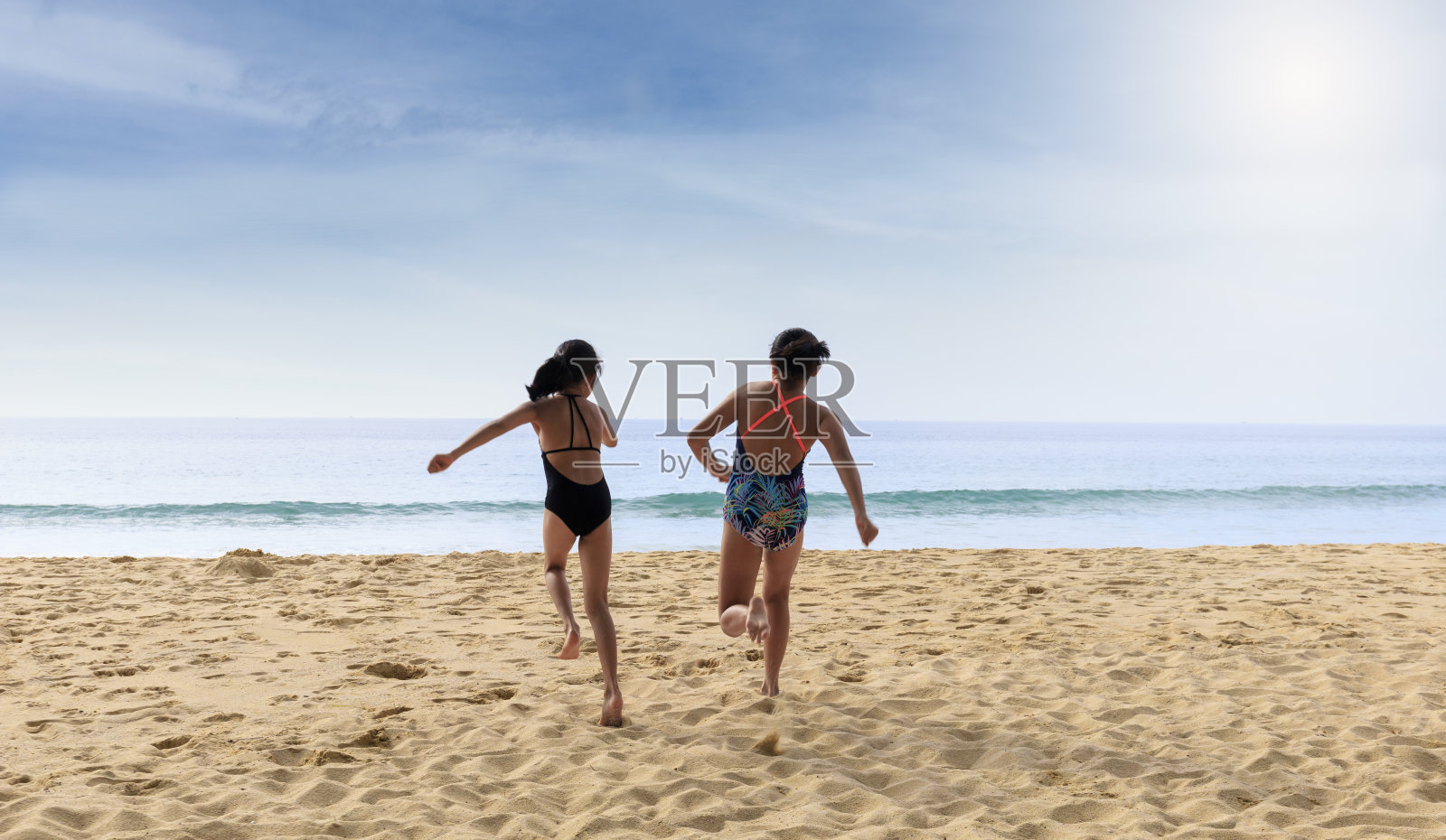 停止运动快乐的两个孩子穿着泳衣从海滩跑向大海。快乐家庭夏日度假理念。两个女孩跑向海滩照片摄影图片