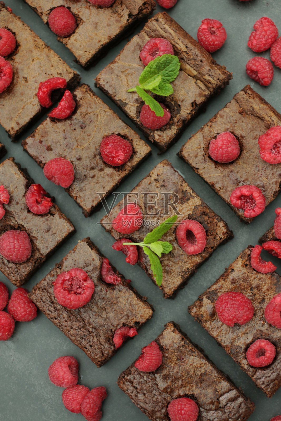 深灰色背景上自制的巧克力和覆盆子布朗尼方块，点缀着覆盆子和薄荷叶，俯瞰照片摄影图片