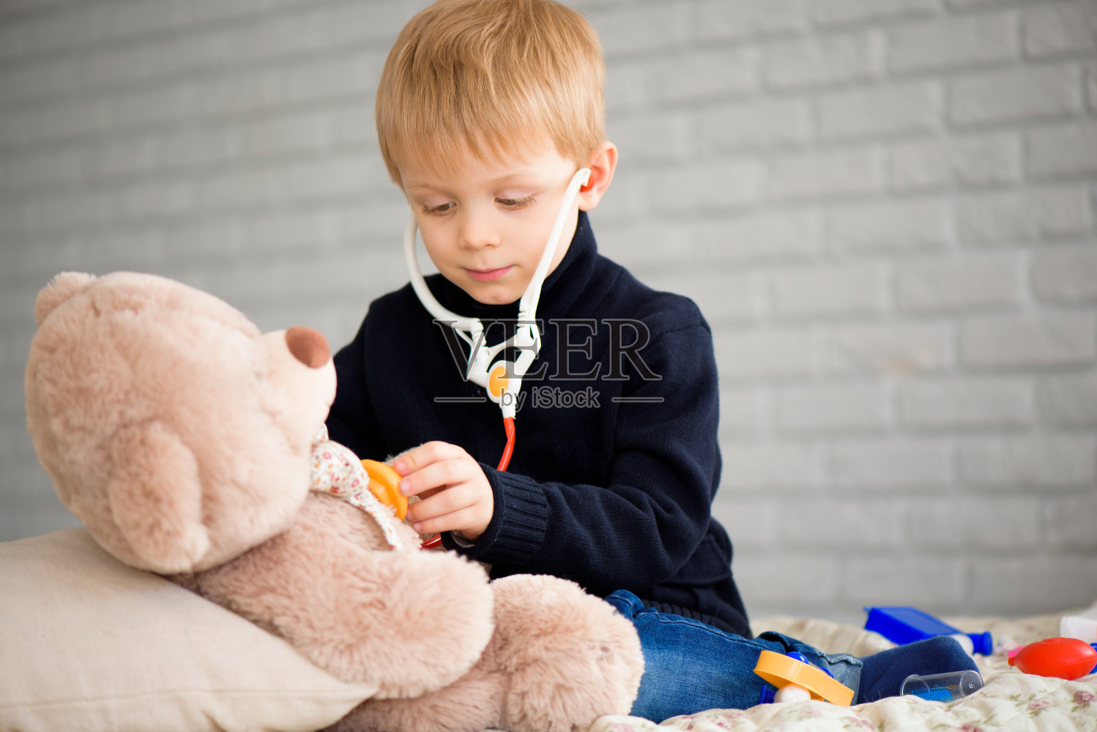 可爱的小男孩装扮成医生在家里玩玩具熊。照片摄影图片