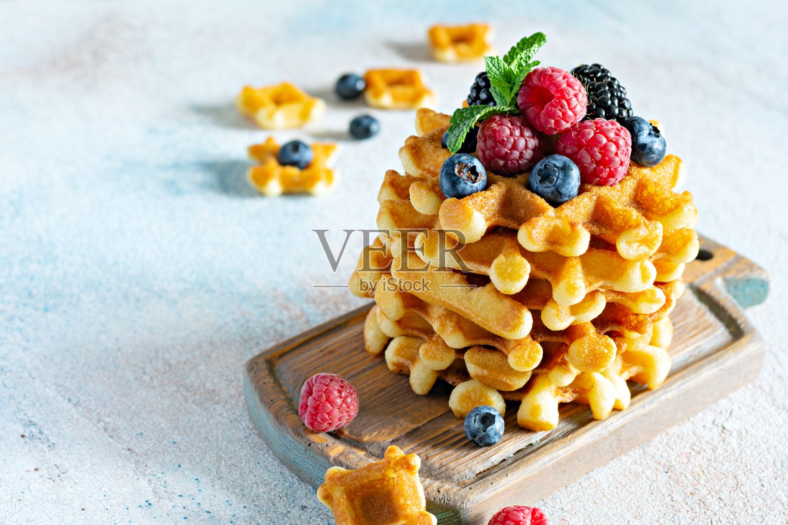 新鲜酥脆的比利时华夫饼配上成熟的浆果(覆盆子、蓝莓、黑莓)、薄荷和糖粉，放在木板上，背景很亮。照片摄影图片