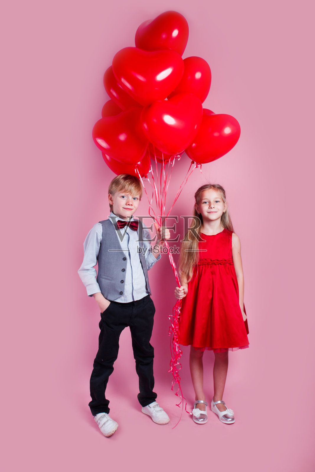 情人节。两个快乐的孩子，粉红色的背景上有心形的气球照片摄影图片