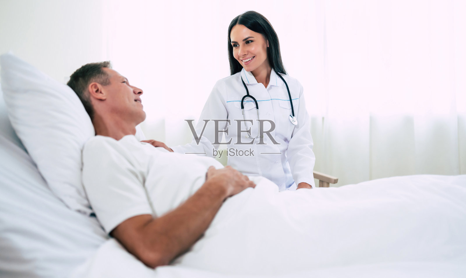 快乐自信的女医生带着听诊器正在病房里与男病人交谈照片摄影图片