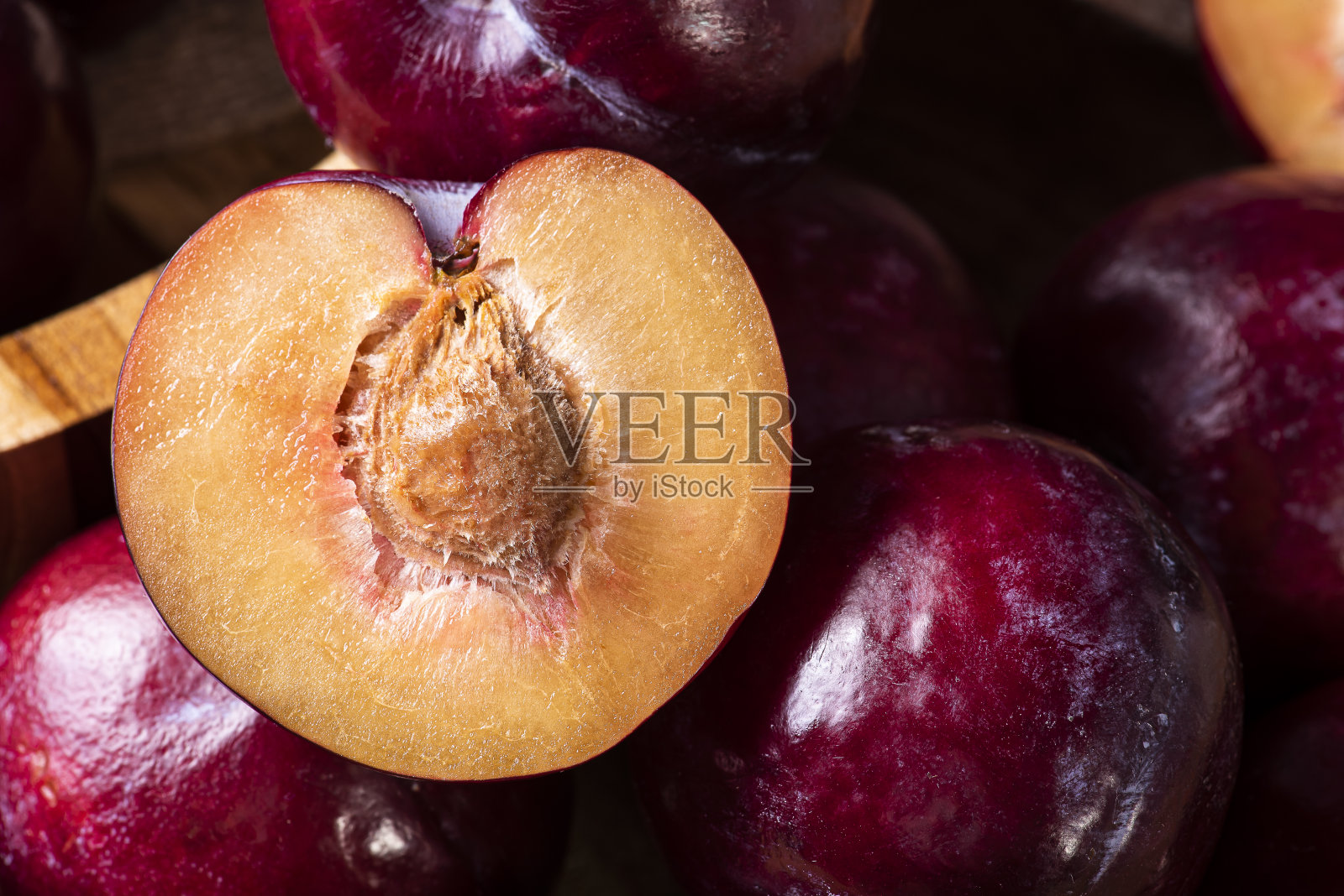 把李子切成两半，在背景上放一些李子。木头的背景。照片摄影图片