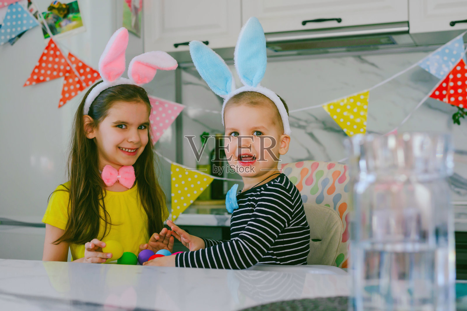 复活节快乐。一对戴着兔耳朵的兄妹一家人正在厨房里为一个明亮的复活节假期做准备。照片摄影图片