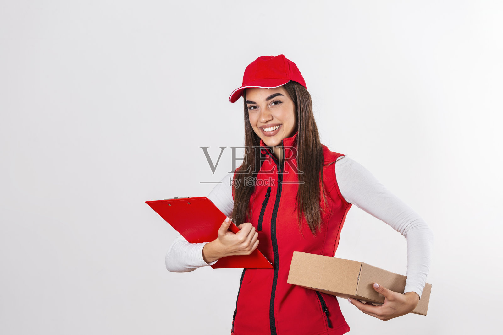 快递员拿着剪贴板送包裹，穿着红色制服微笑着送包裹。美丽的年轻女子专业信使孤立在白色的背景照片摄影图片