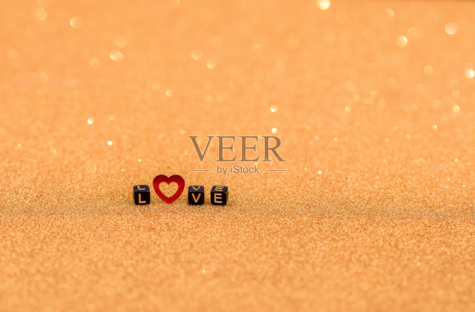 “爱”这个词是木制的字母和一颗红心，在金色的背景上点缀着亮片。散焦和选择性散焦照片摄影图片