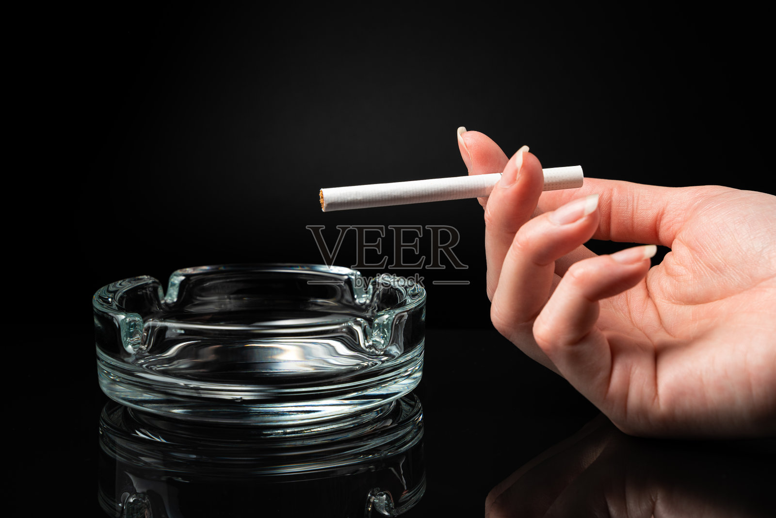一个女人的手里拿着香烟，旁边是一个烟灰缸，背景是黑色的照片摄影图片