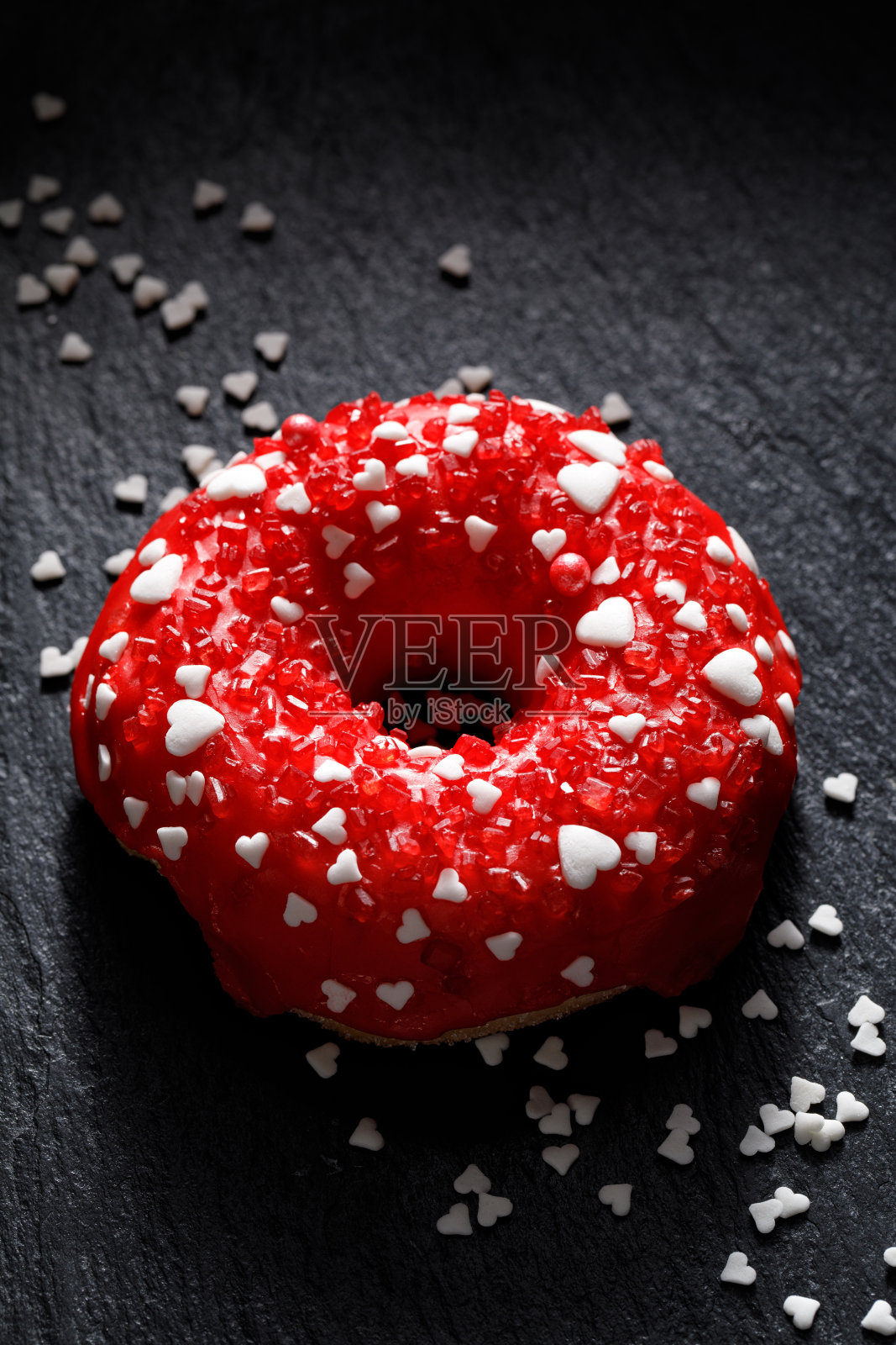 情人节甜甜圈，红色甜釉和各种点缀在黑色背景上照片摄影图片