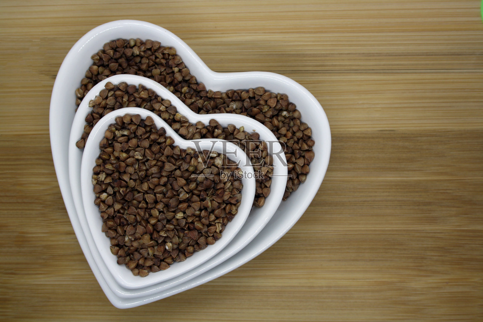 木背景上的心形碗里装着荞麦。照片摄影图片