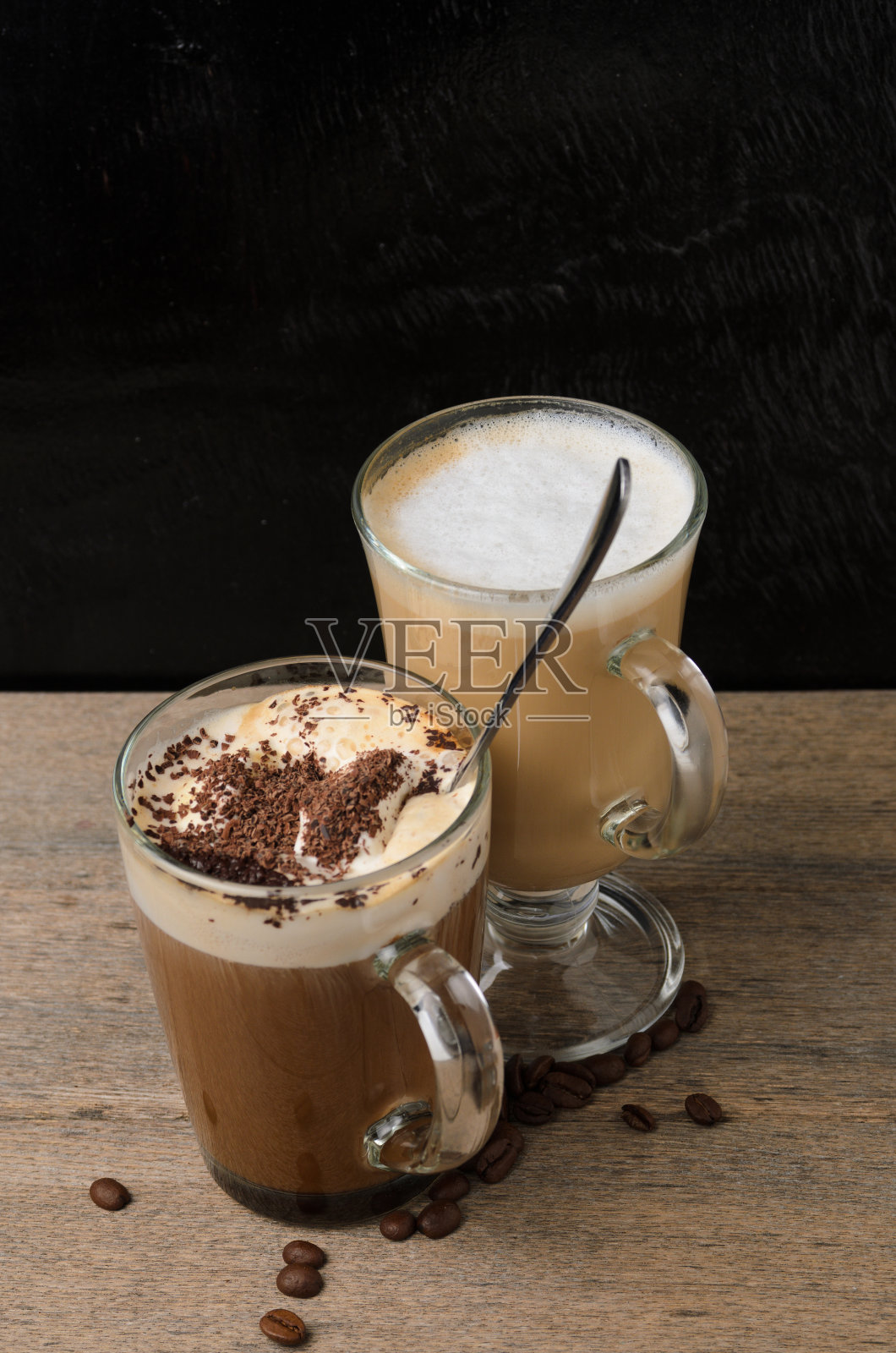 木桌上放着两个杯子，一杯卡布奇诺和一杯冰巧克力，背景是黑色的照片摄影图片