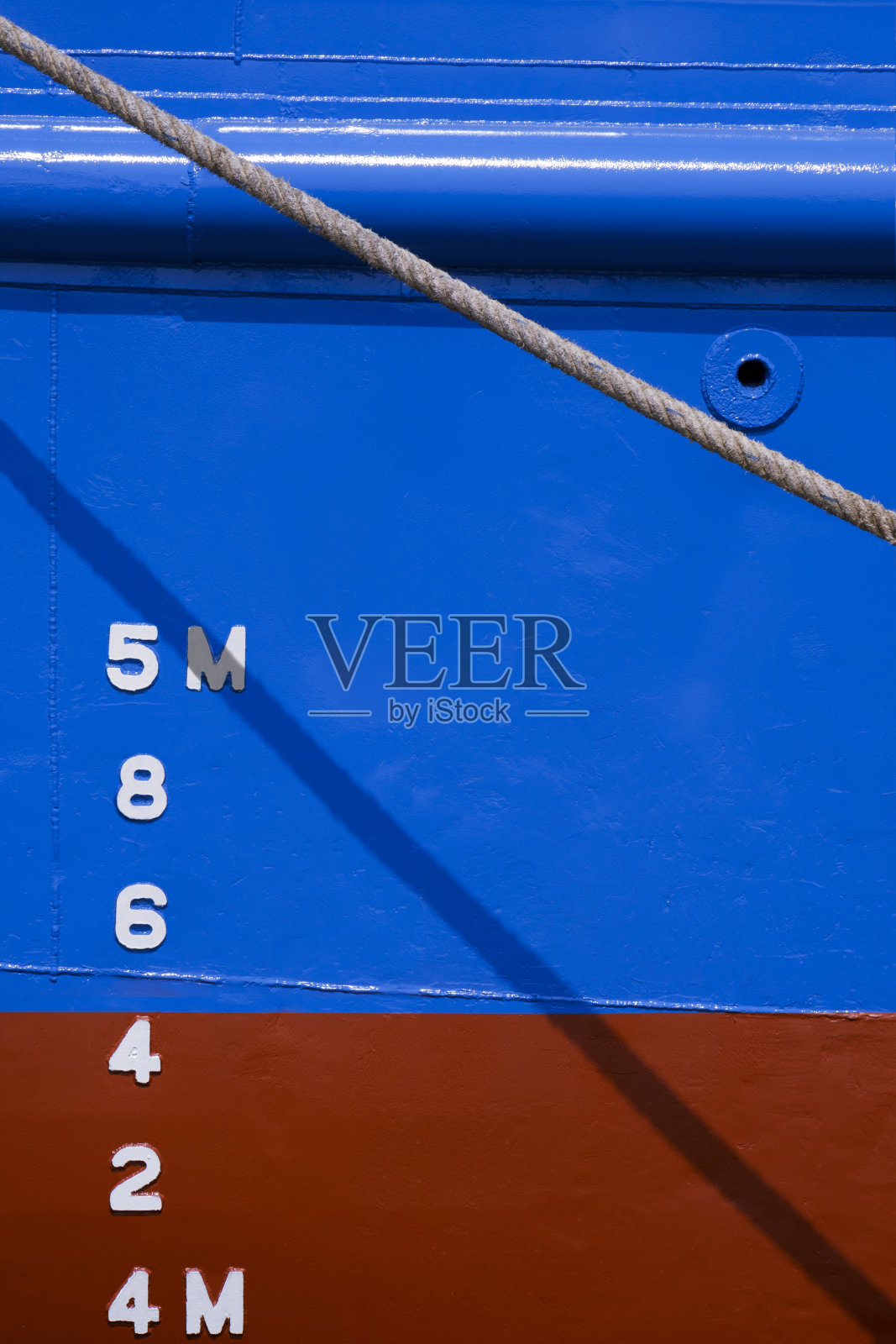 在蓝色和红色的防锈船壳的侧面，旧的巨大纤维绳后面的吃水标记号码照片摄影图片