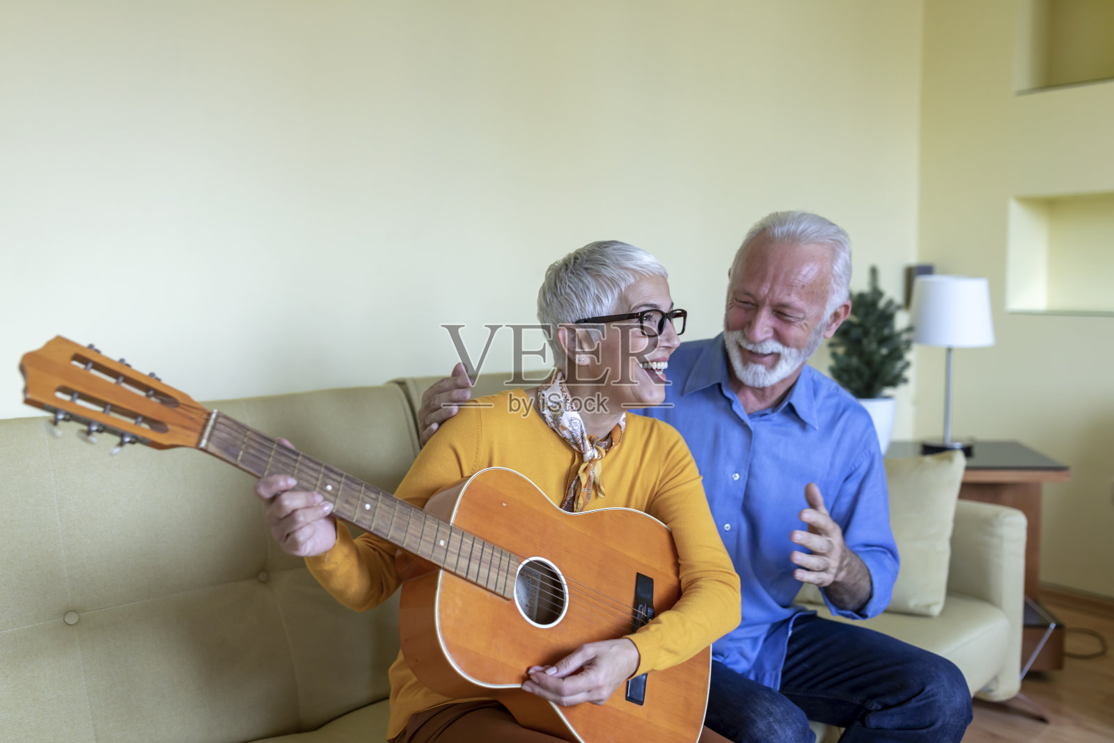 一位快乐的退休老人正在为她喜欢轻松音乐的英俊的丈夫弹吉他。照片摄影图片