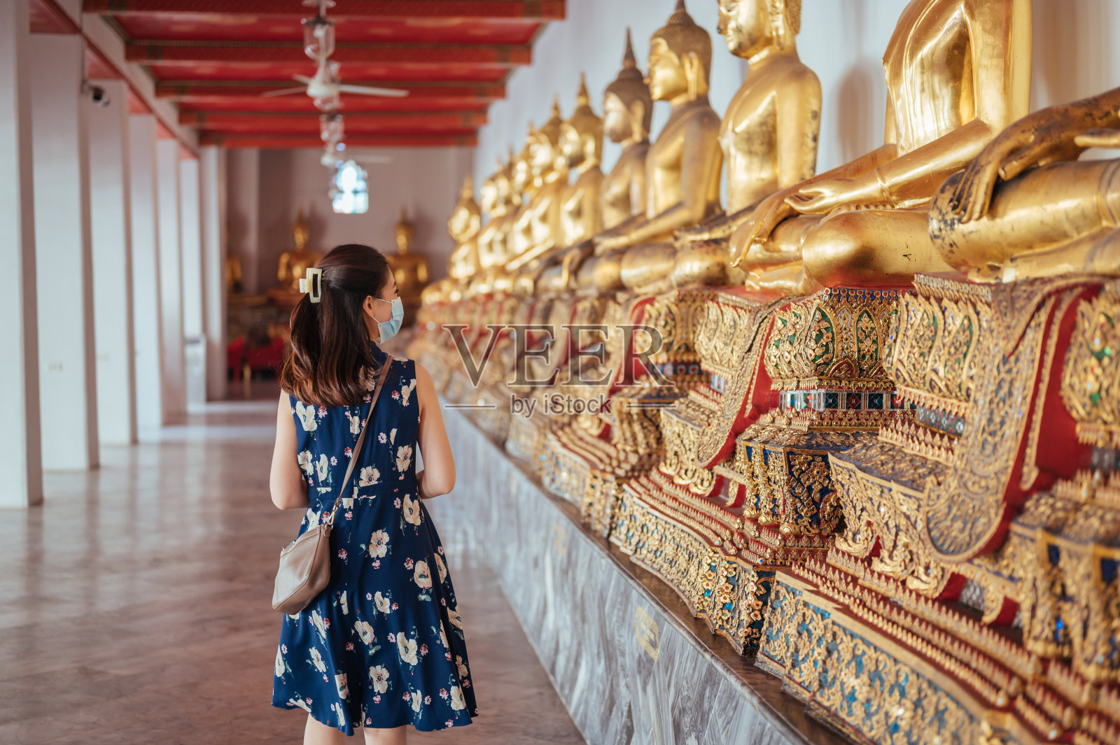 后视图年轻的亚洲游客快乐的女人享受旅游当地旅游祈祷在佛寺金色佛像曼谷，泰国。东南亚戴口罩照片摄影图片