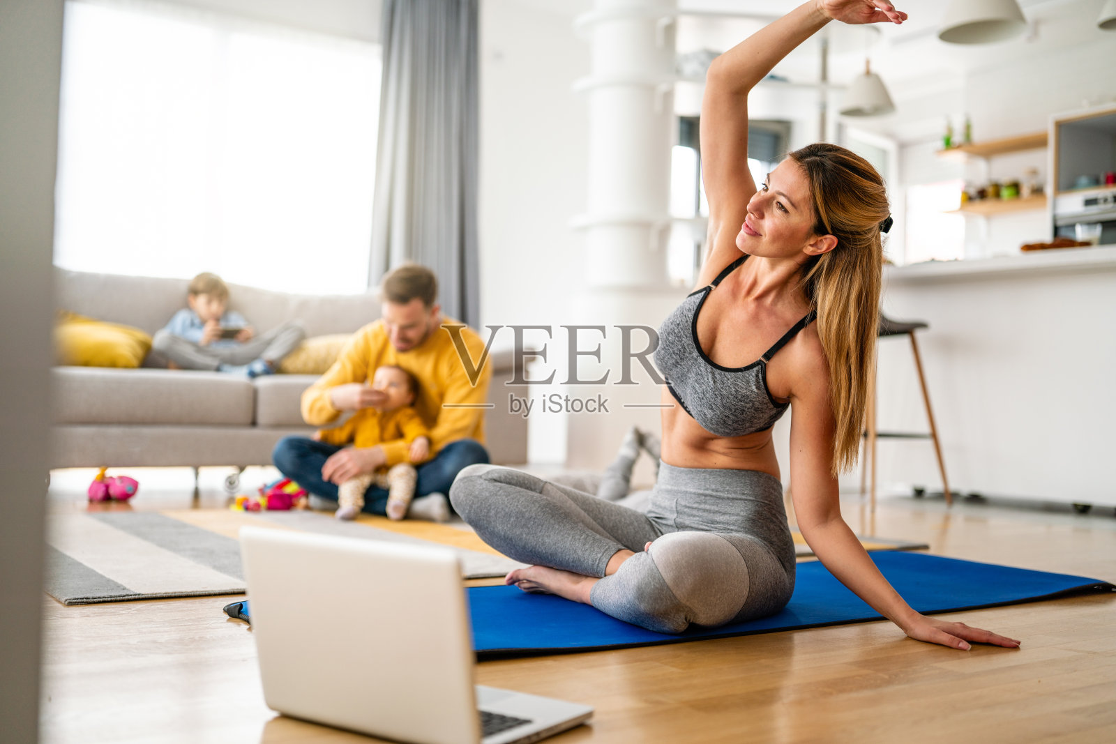 年轻女子，母亲在客厅锻炼身体，父亲在后台和孩子们玩耍。照片摄影图片