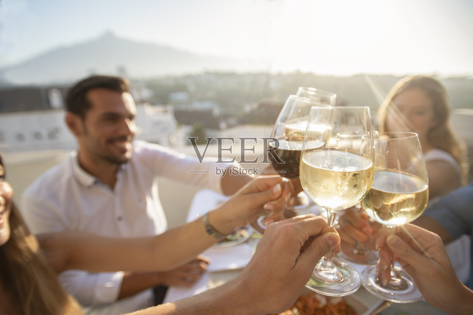 一群朋友在户外用餐。他们用葡萄酒祝酒庆祝。照片摄影图片