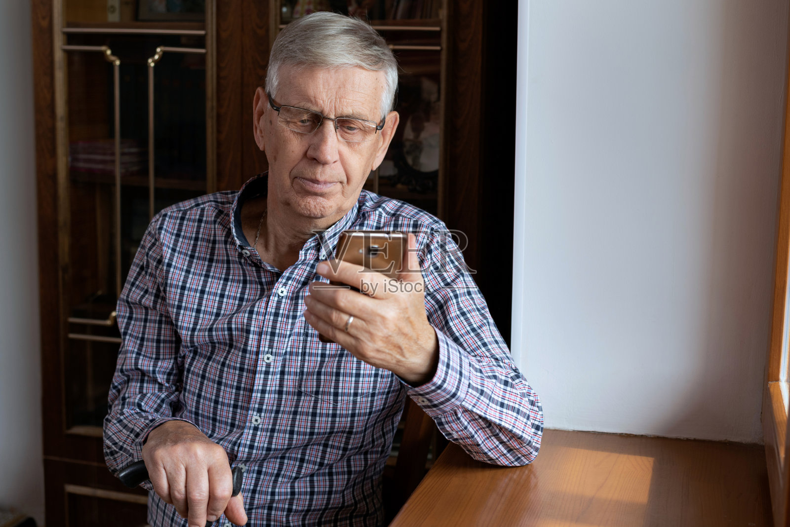 一位心满意足的老人坐在家里，看着手机，上网。照片摄影图片