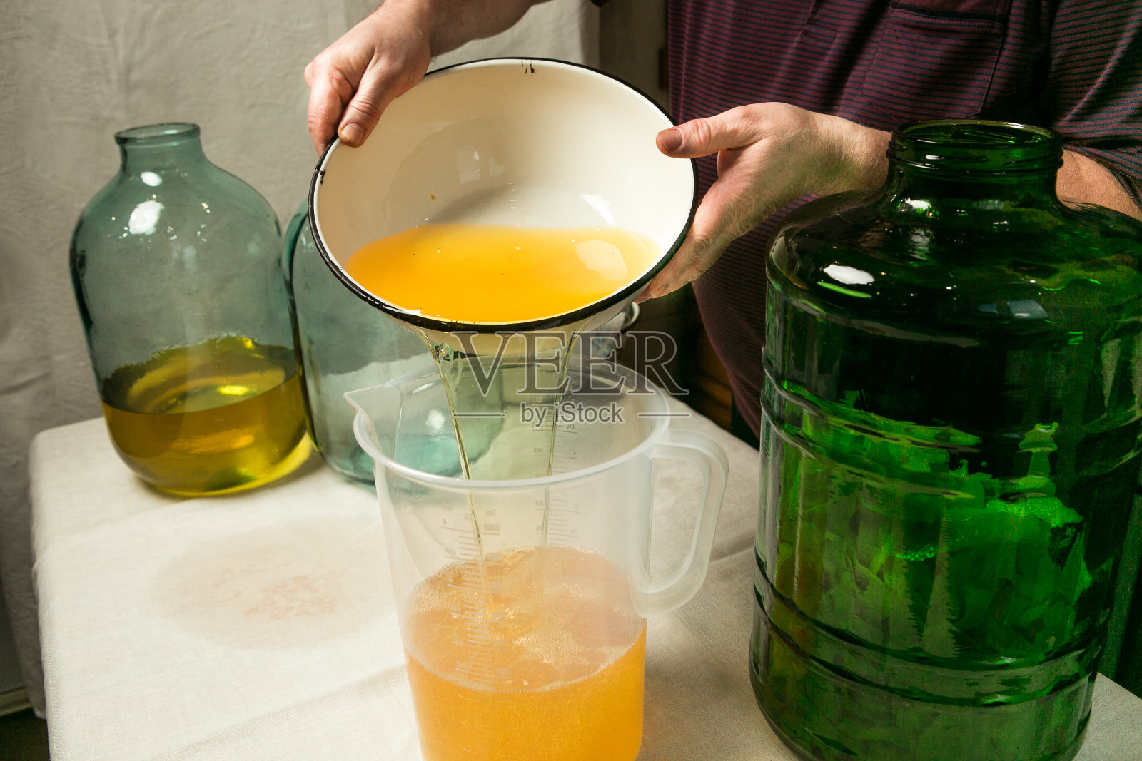 在家里制作柠檬酒的过程。该男子排水并过滤浸有柠檬皮的酒精，并测量与糖浆混合所需的液体体积。照片摄影图片