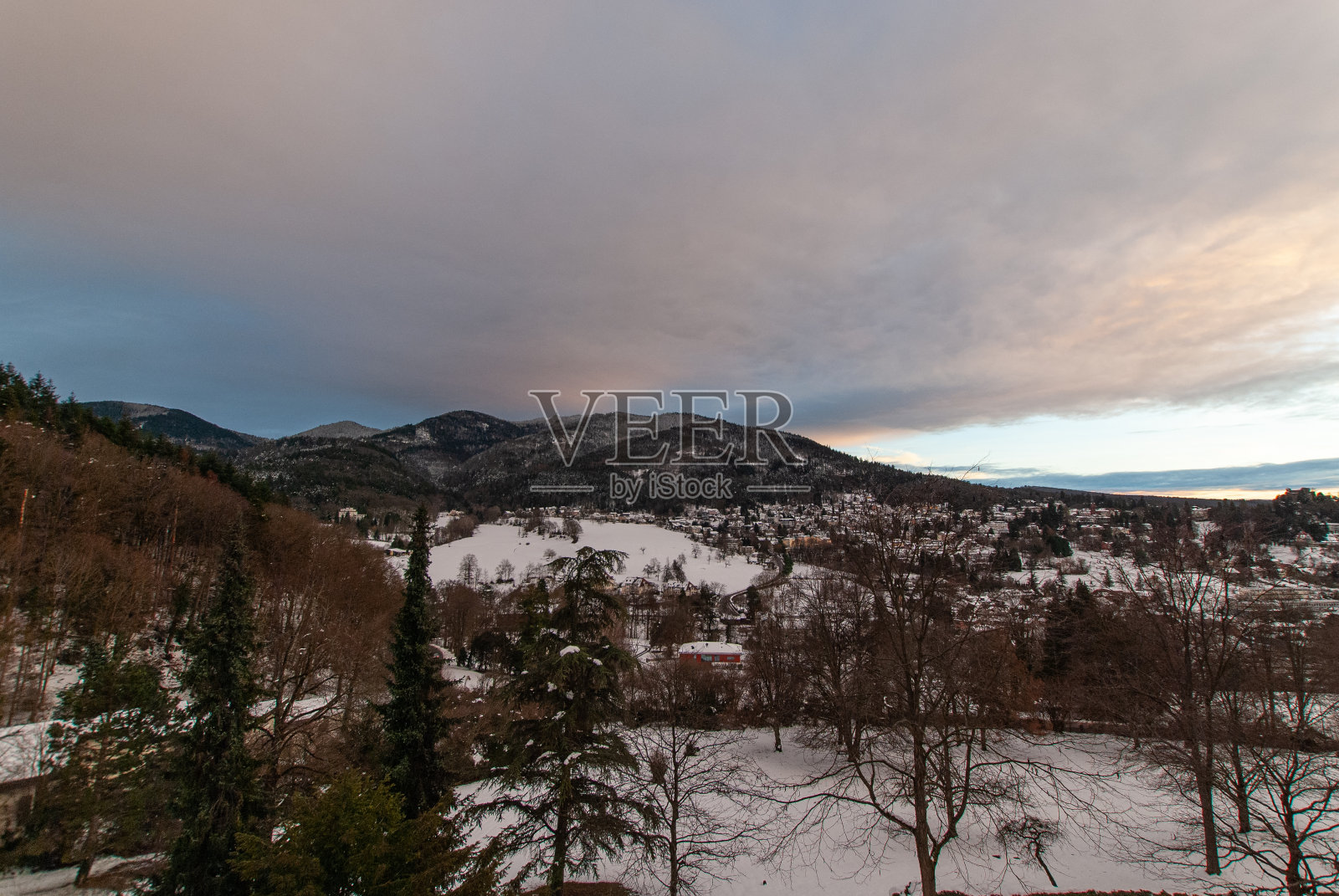 傍晚的时候，巴登韦勒镇和森林茂密的山丘上，乌云在天空中散开。照片摄影图片