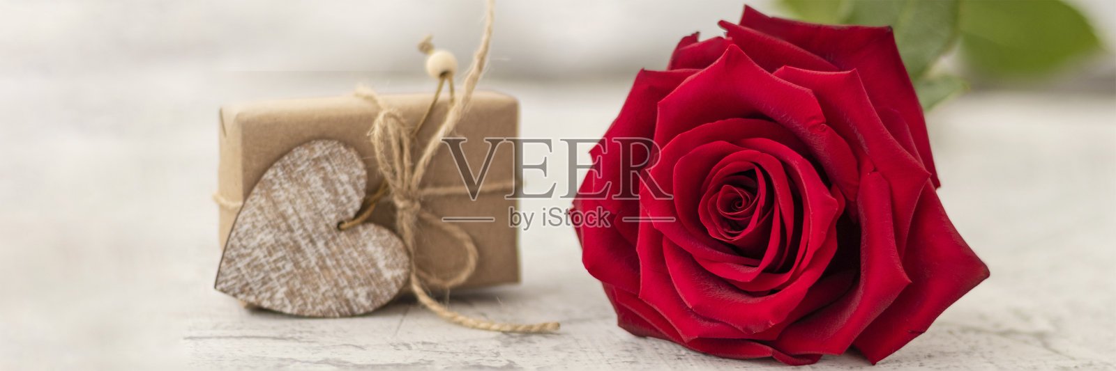 用牛皮纸包着礼物的横幅，旁边是白石背景上的红玫瑰。浪漫的情人节礼物，有文字空间。求婚的概念照片摄影图片