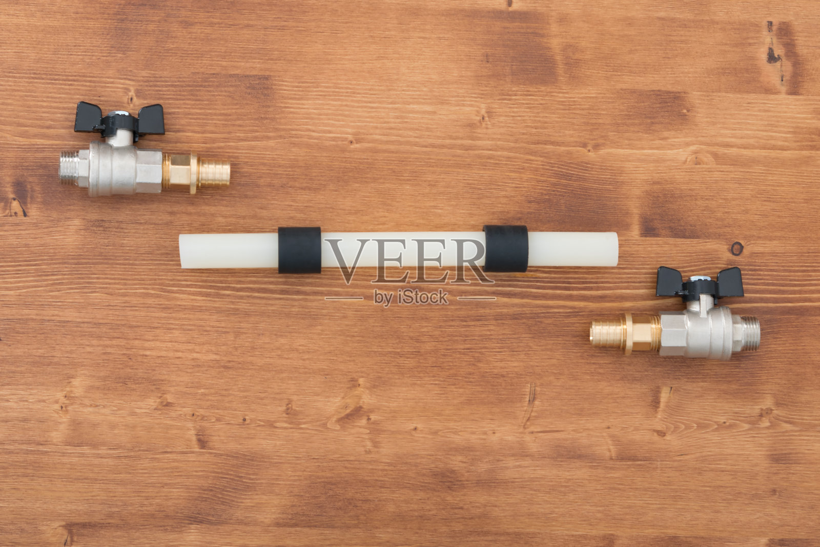 在木制的表面上，有一根带有两个黑色固定环的塑料管和用来固定水的水龙头照片摄影图片