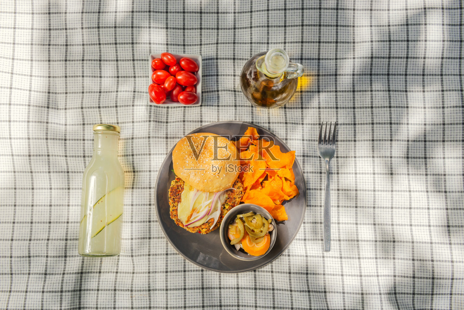 夏日野餐的气氛，草坪上的桌布上放着健康食品和水果饮料。平的食物。橄榄油，沙拉，三明治，藜麦沙拉，素食汉堡。照片摄影图片