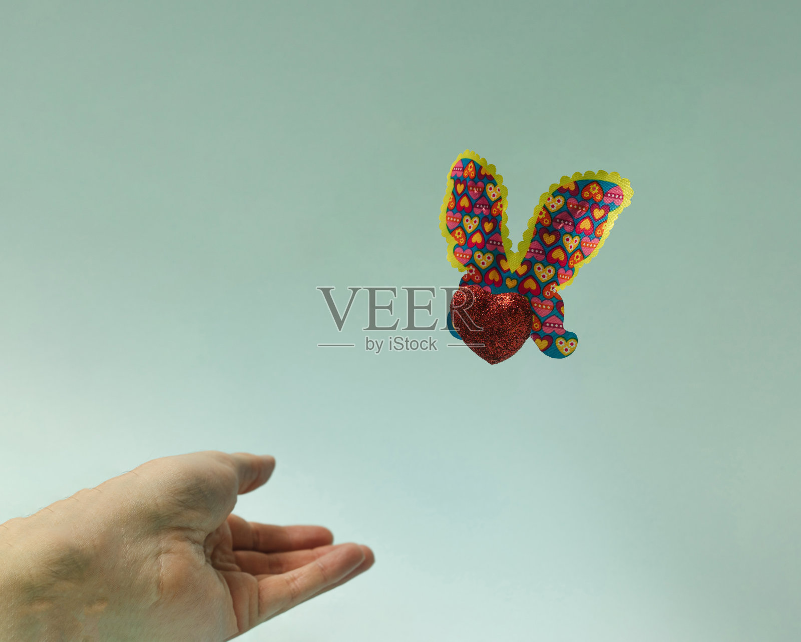 闪闪发光的心形身体和蝴蝶的翅膀-蝴蝶的手释放。漂亮的浅绿色背景。照片摄影图片