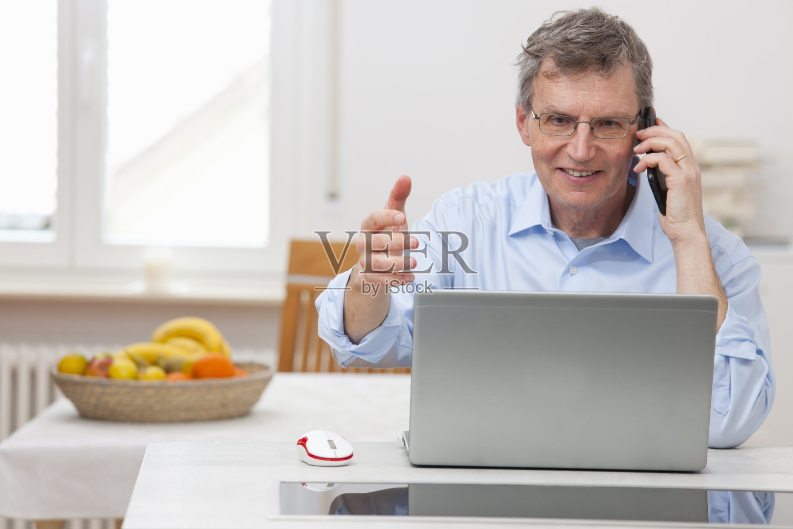 微笑的商人在家里办公，在笔记本电脑前用智能手机聊天照片摄影图片