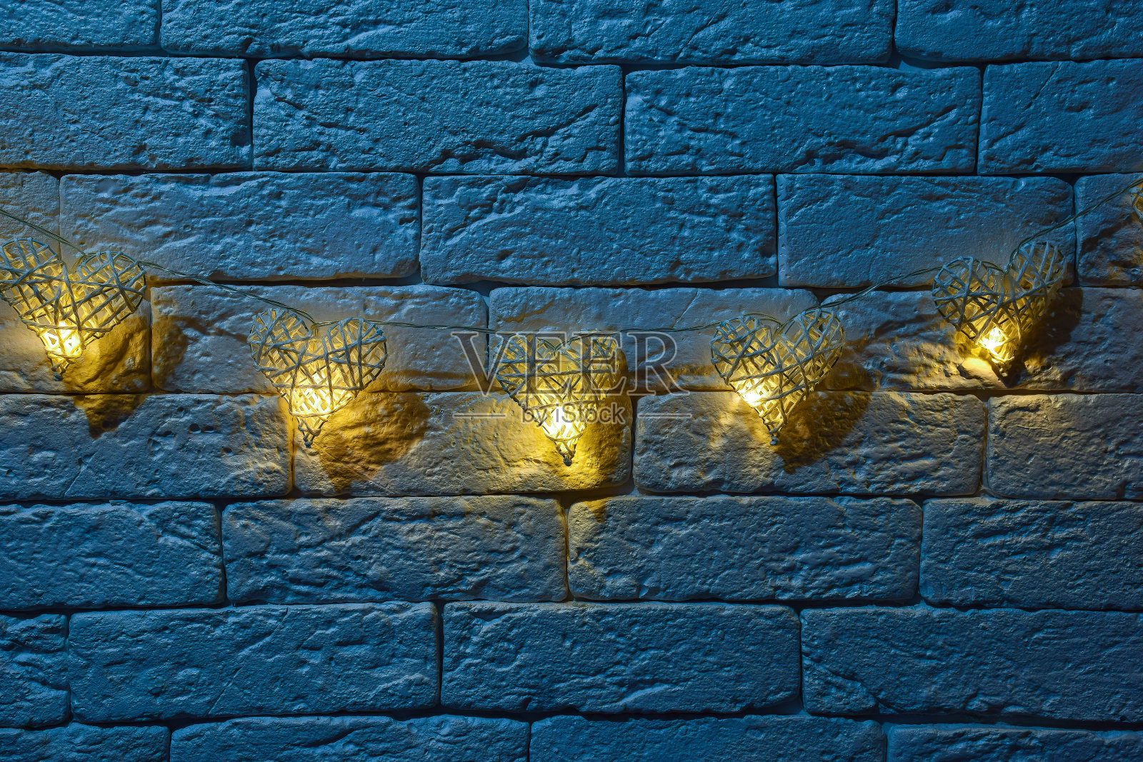 装饰砖墙上挂着五个手工制作的柳条心形装饰灯。上面和下面都有不同节日的题字。照片摄影图片