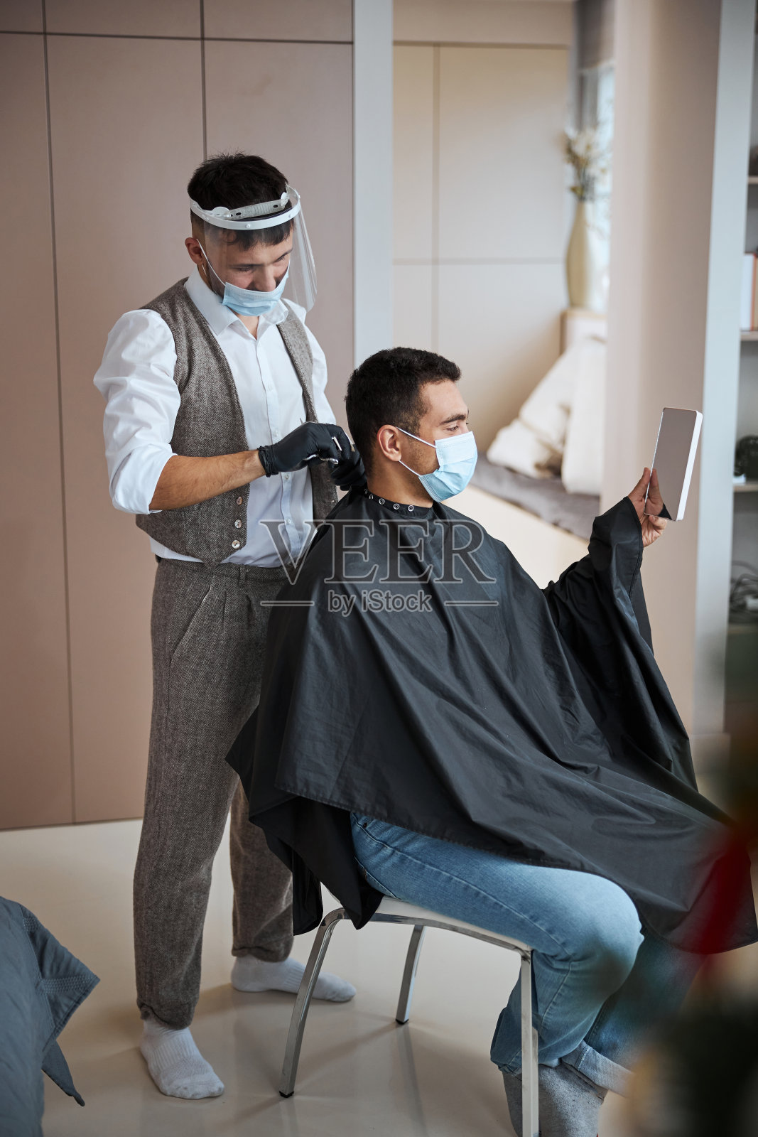 英俊的印度男子看着镜子里的映像，而理发师站在旁边照片摄影图片