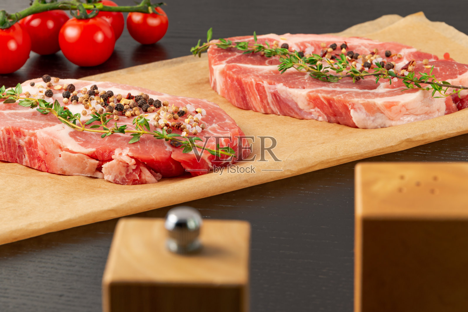 新鲜切好的生猪肉加香料和百里香放在羊皮纸上。旁边是熟西红柿和盐瓶照片摄影图片