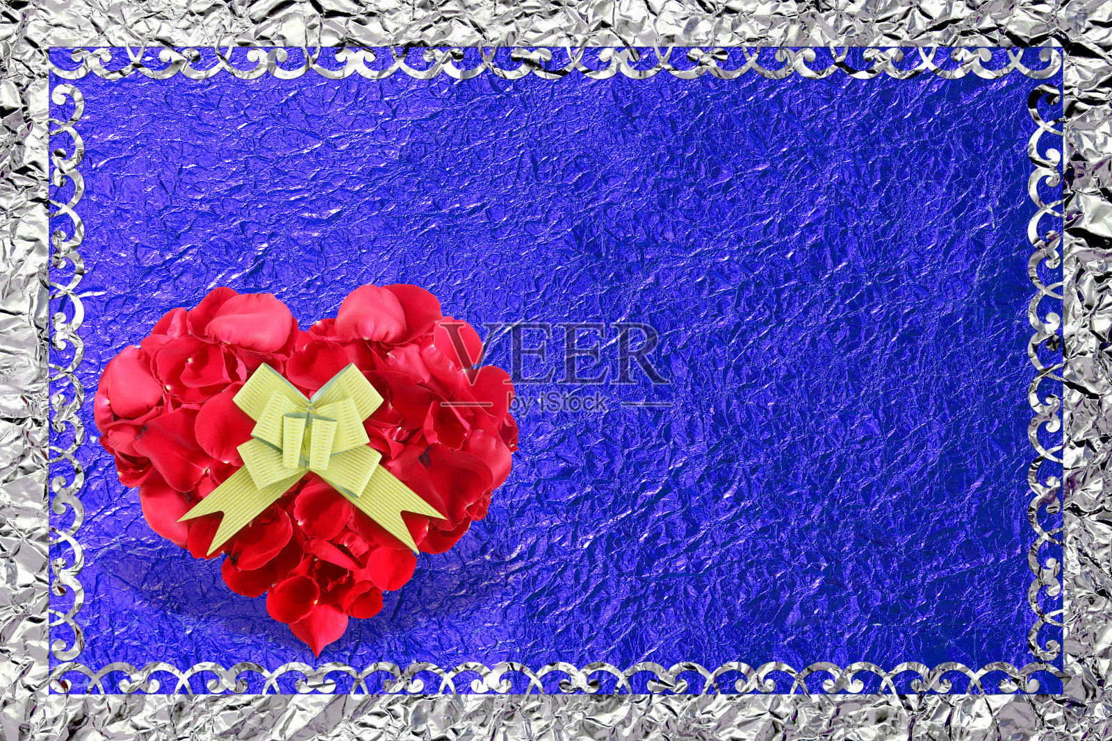 心形玫瑰花瓣与金色蝴蝶结在蓝色箔的背景。照片摄影图片