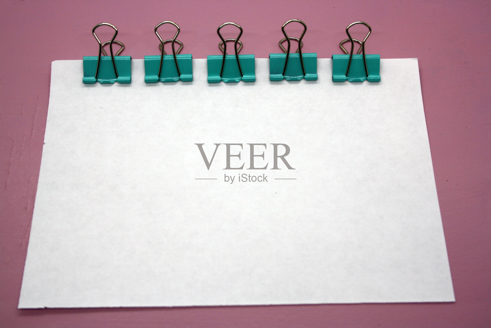 粉色背景上的蓝色回形针。照片摄影图片