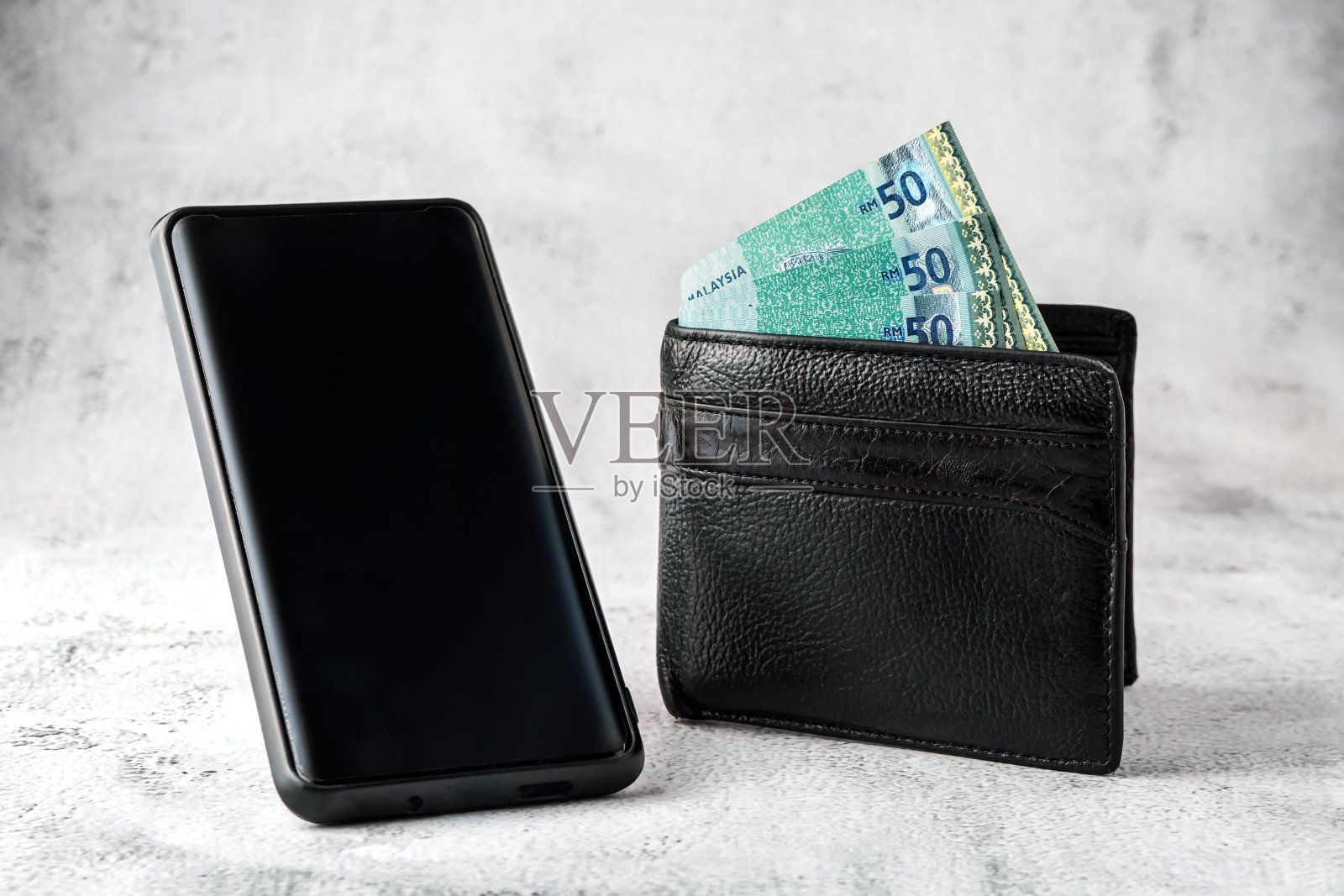 黑色钱包里的马来西亚林吉特钞票和黑色智能手机上的垃圾白色背景照片摄影图片
