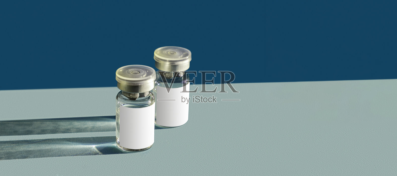 蓝色玻璃小瓶，液体蓝色背景，有坚硬的阴影。可能的冠状病毒疫苗或美容治疗的剂量，痤疮面部血清。空模型。文本空间,横幅照片摄影图片