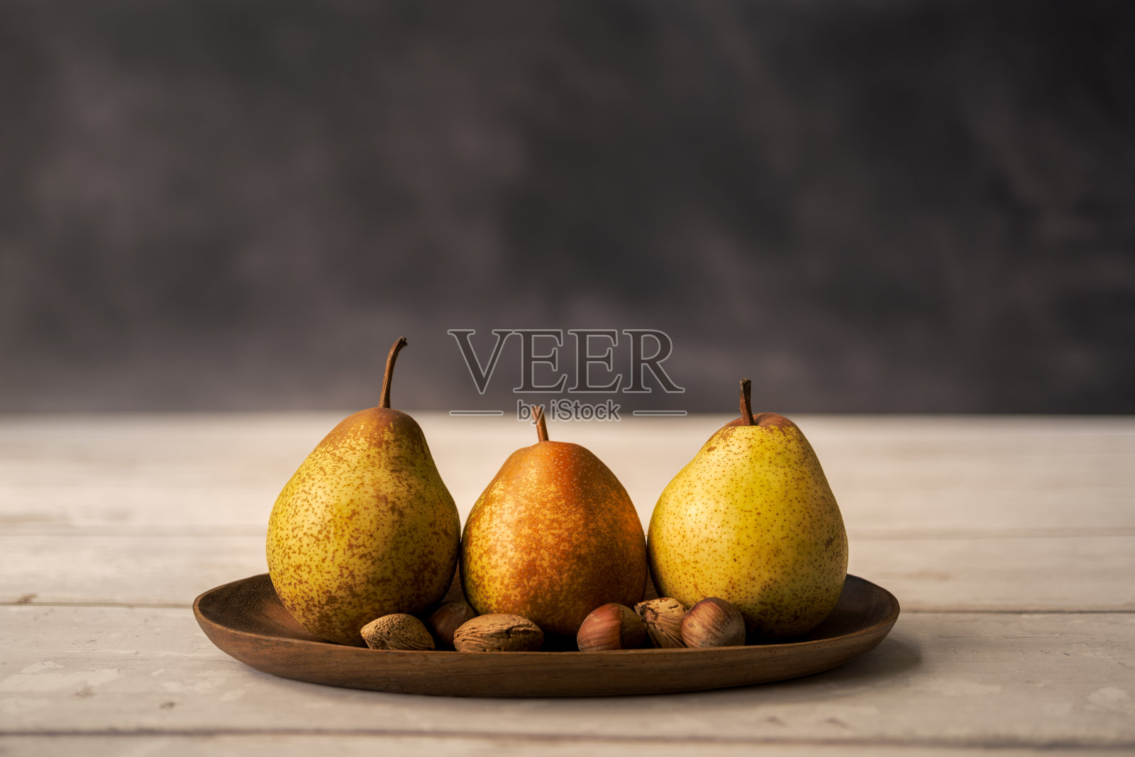 三个梨和坚果在一个木杯孤立在黑暗的背景。健康饮食的概念照片摄影图片