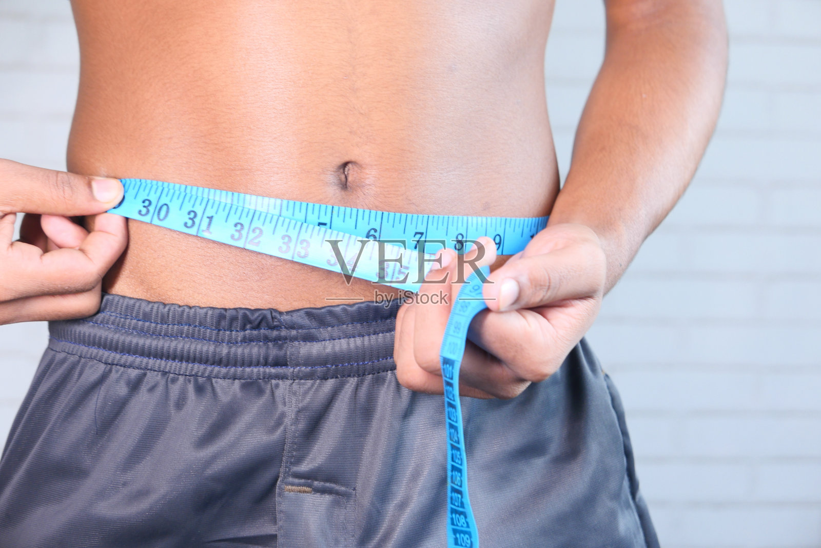 一个年轻人正在用卷尺测量自己的腰围。照片摄影图片