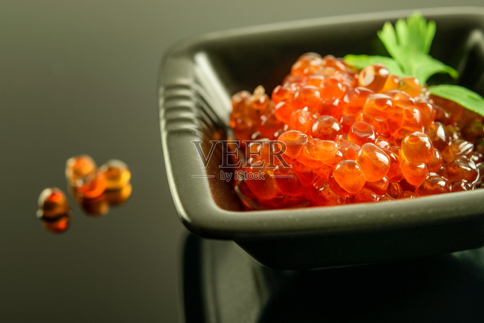 新鲜的红鱼子酱在黑色的碗上反射的背景。健康的海鲜，奢华，美味。照片摄影图片