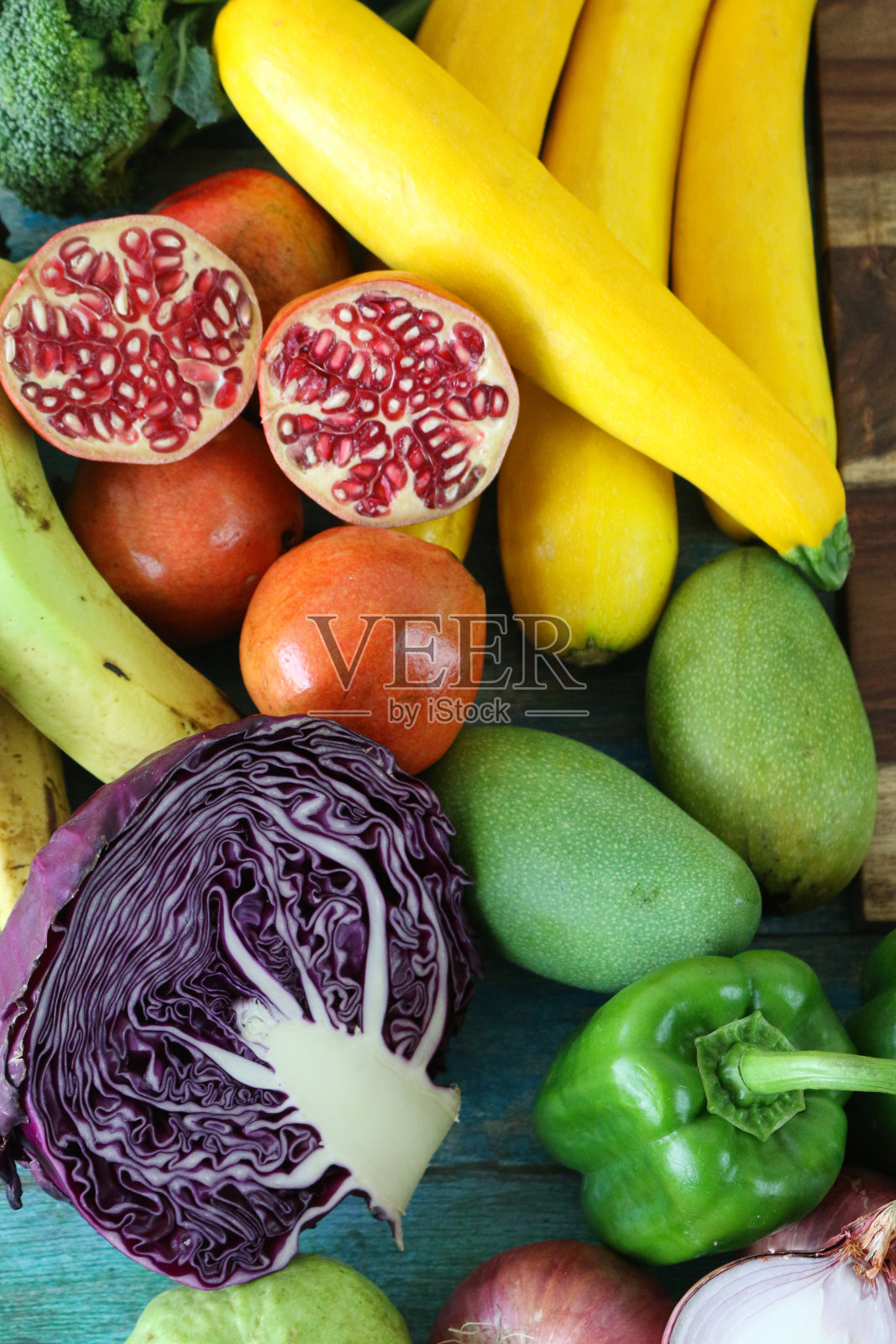 彩虹的特写，展示多种颜色的水果和蔬菜，包括紫甘蓝、绿黄瓜、苦瓜、青豆、黄胡椒、黄西葫芦/西葫芦、橙胡萝卜、橙、番茄、红甜椒、石榴片照片摄影图片